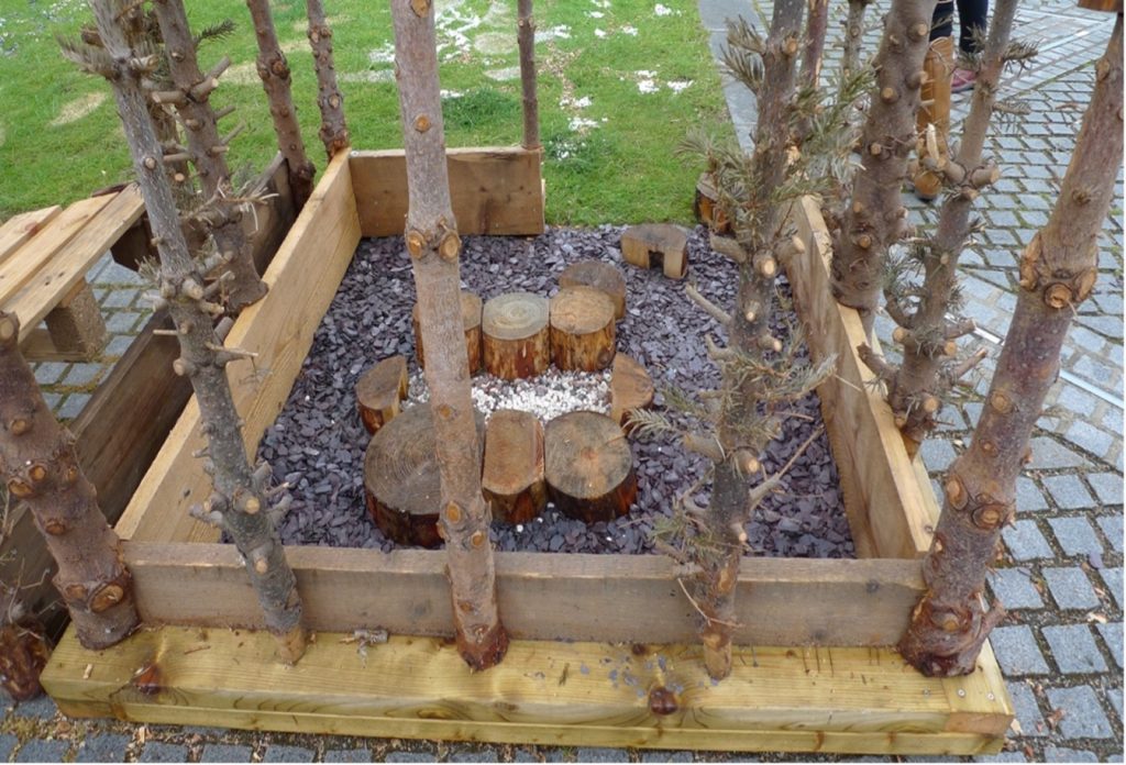 Small enclosed section with upright tree trunks surrounding cut log stools arranged in a circle.