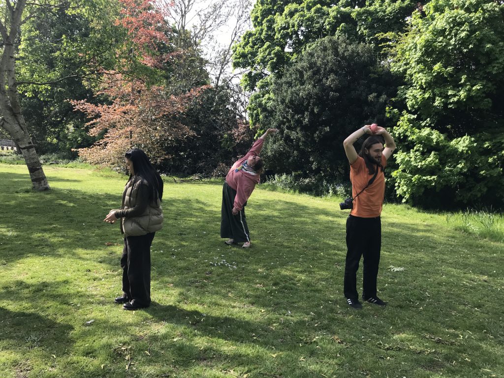 Three people in a sunny park, standing apart and performing during a sensory workshop.