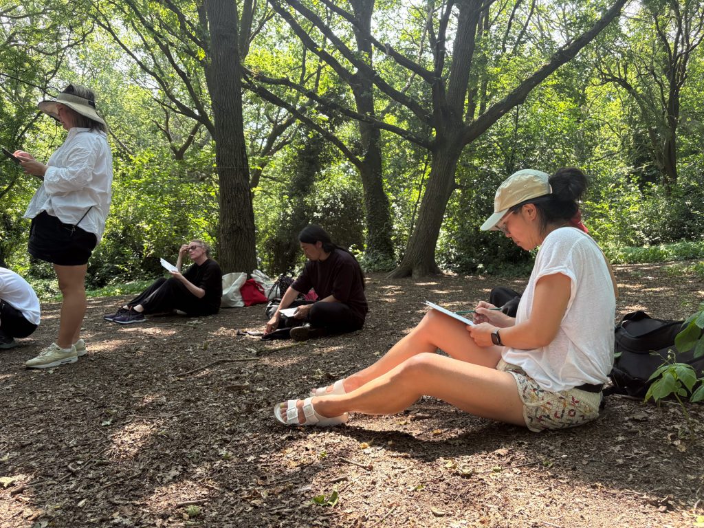 A participant sitting in tall grass overlooking trees and the London skyline, taking a quiet moment to observe the landscape.