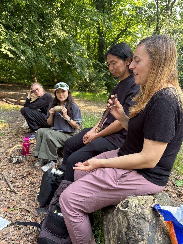 Participants sitting on logs in a forest circle, engaged in conversation while holding small natural samples.