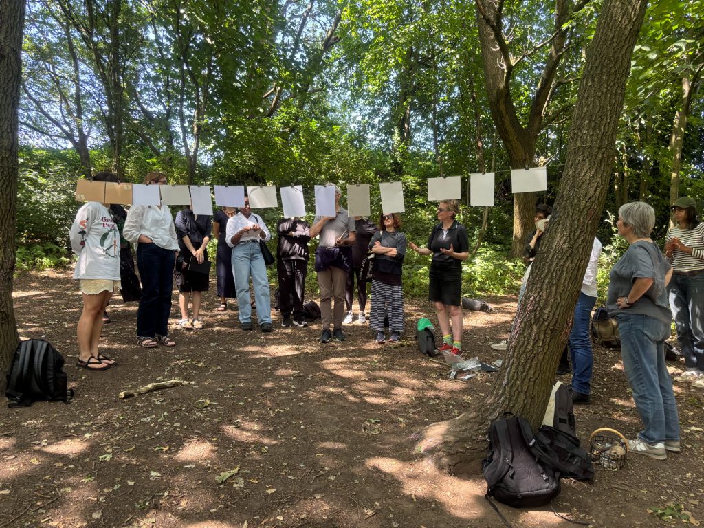 Participants gather next to drawings hung on a string between trees for a woodland gallery.